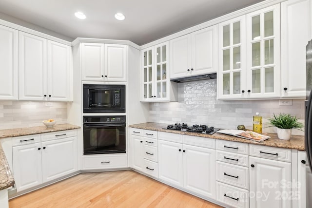 kitchen featuring white cabinets, light stone counters, black appliances, custom range hood, and light hardwood / wood-style flooring