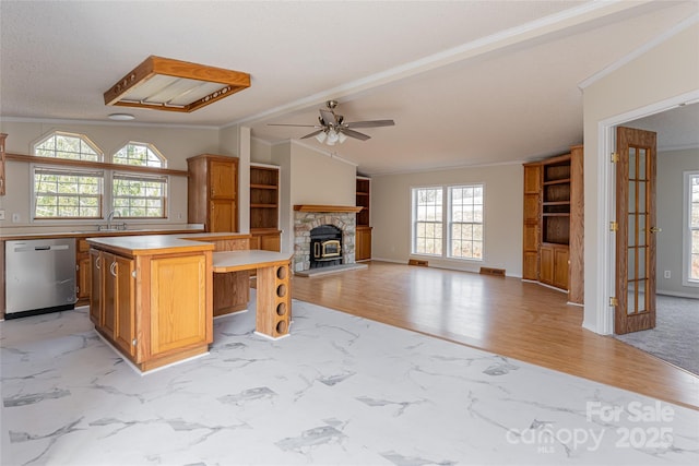 kitchen featuring a kitchen island, a fireplace, stainless steel dishwasher, crown molding, and light wood-type flooring