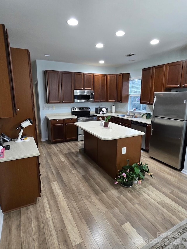 kitchen with sink, appliances with stainless steel finishes, dark brown cabinets, a kitchen island, and light wood-type flooring