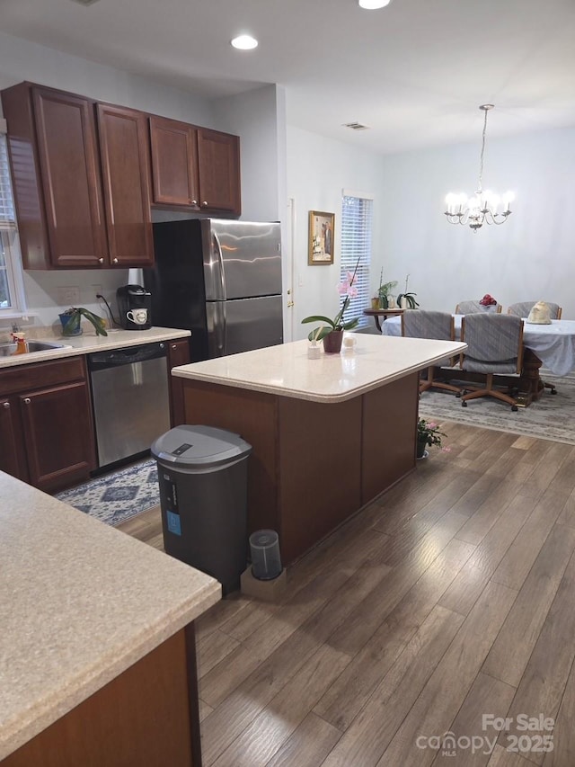 kitchen with a kitchen island, appliances with stainless steel finishes, decorative light fixtures, dark brown cabinetry, and dark wood-type flooring