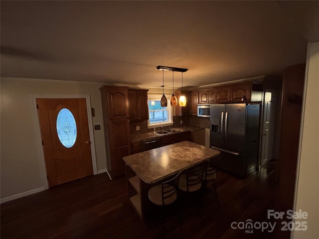 kitchen featuring dark wood-type flooring, sink, decorative light fixtures, a center island, and stainless steel appliances