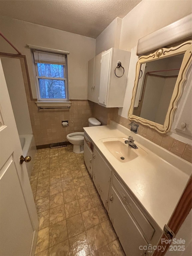 bathroom with vanity, toilet, a textured ceiling, and tile walls