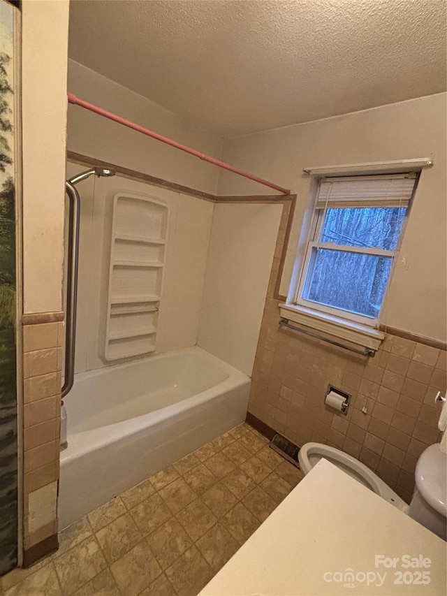 bathroom with shower / washtub combination, toilet, a textured ceiling, and tile walls