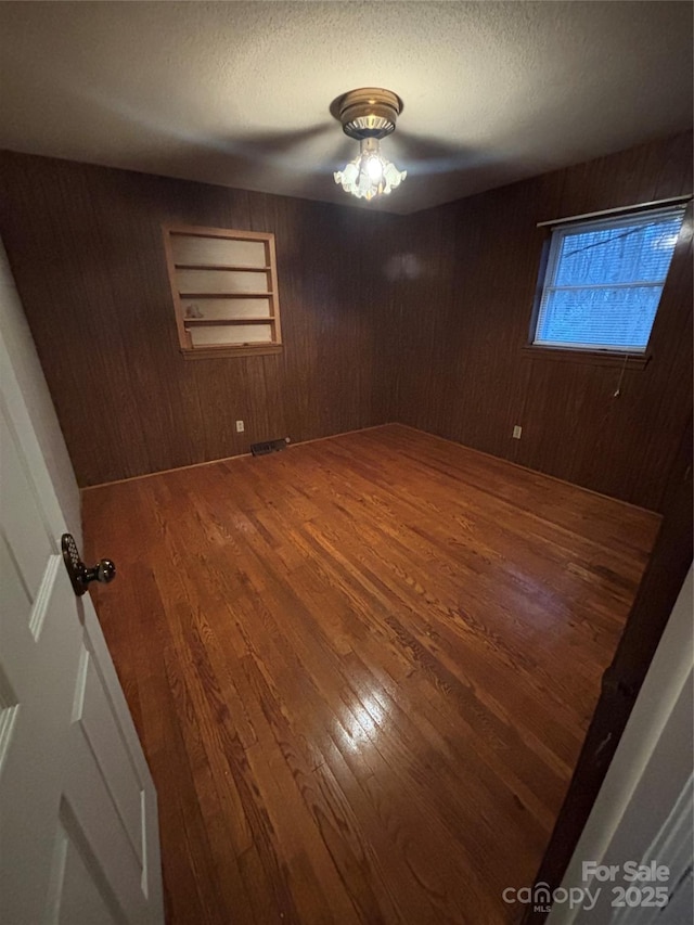 unfurnished room featuring hardwood / wood-style flooring, a textured ceiling, and wood walls