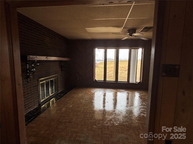 unfurnished living room with dark parquet flooring, a paneled ceiling, ceiling fan, and a fireplace