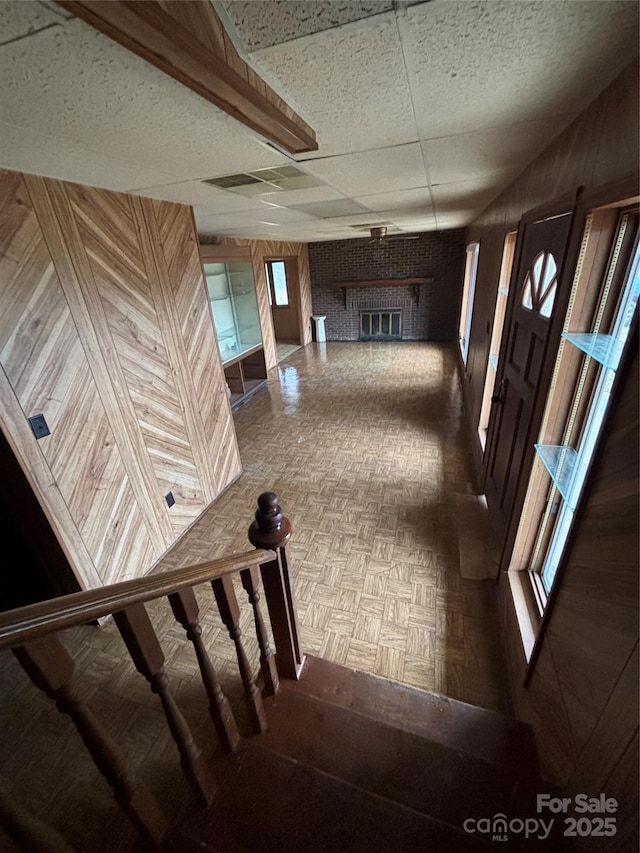 interior space with a brick fireplace, parquet flooring, wooden walls, and a paneled ceiling