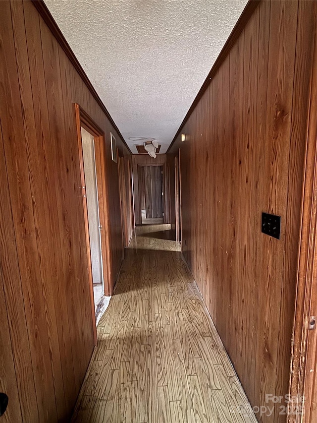 hall with crown molding, wooden walls, light hardwood / wood-style floors, and a textured ceiling