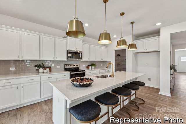 kitchen with sink, hanging light fixtures, appliances with stainless steel finishes, an island with sink, and white cabinets