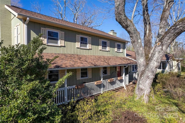 back of house featuring a shingled roof, brick siding, a porch, and a chimney