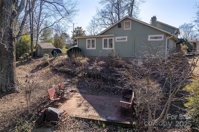 back of house with an outbuilding, a patio, a chimney, and a storage unit