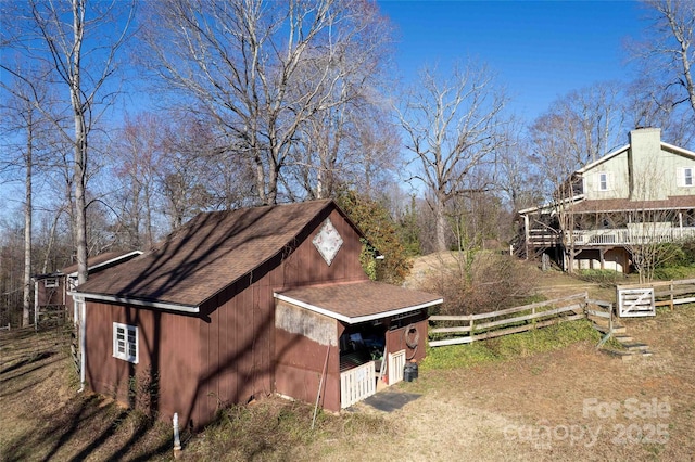 view of side of property with roof with shingles, fence, and an outdoor structure