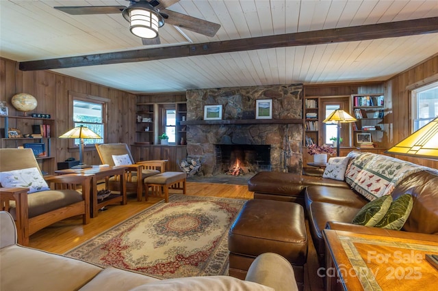 living room featuring a fireplace, beamed ceiling, wooden walls, and wood finished floors