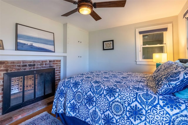 bedroom with a brick fireplace, ceiling fan, and wood finished floors