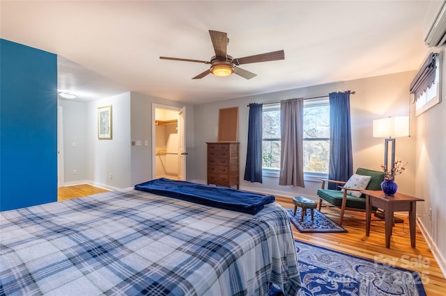 bedroom featuring a ceiling fan, an AC wall unit, baseboards, and wood finished floors