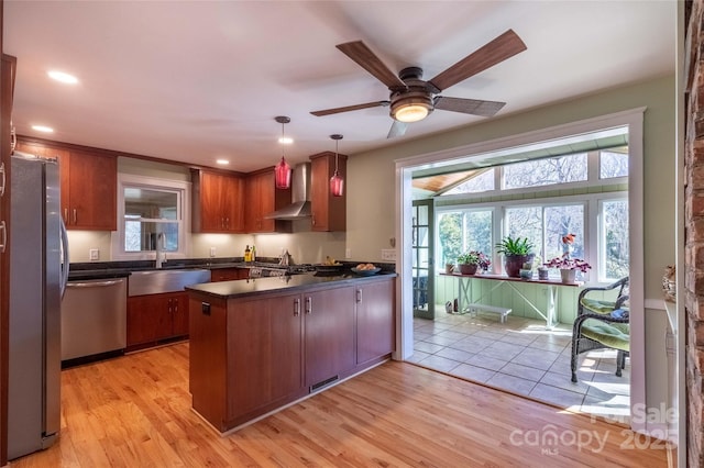 kitchen featuring dark countertops, wall chimney exhaust hood, appliances with stainless steel finishes, a peninsula, and a sink