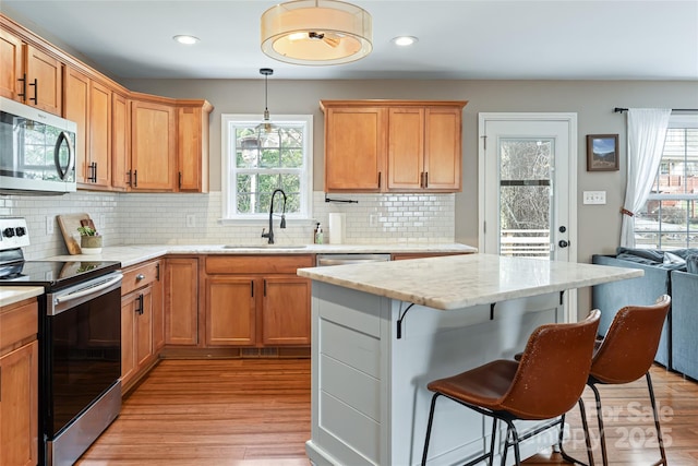 kitchen featuring a breakfast bar area, stainless steel appliances, hanging light fixtures, light wood-style floors, and a sink