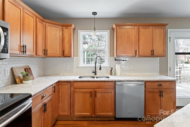 kitchen featuring light stone counters, hanging light fixtures, backsplash, appliances with stainless steel finishes, and a sink