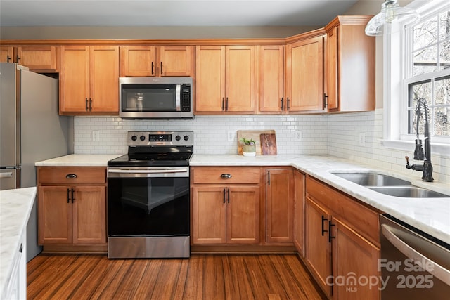 kitchen featuring dark wood finished floors, decorative backsplash, stainless steel appliances, and a sink