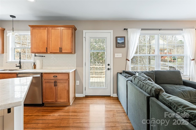 kitchen featuring light wood-style floors, light countertops, decorative backsplash, dishwasher, and pendant lighting