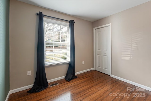 unfurnished bedroom featuring a closet, visible vents, baseboards, and wood finished floors