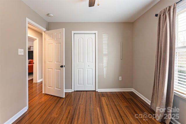 unfurnished bedroom with ceiling fan, baseboards, dark wood finished floors, and a closet