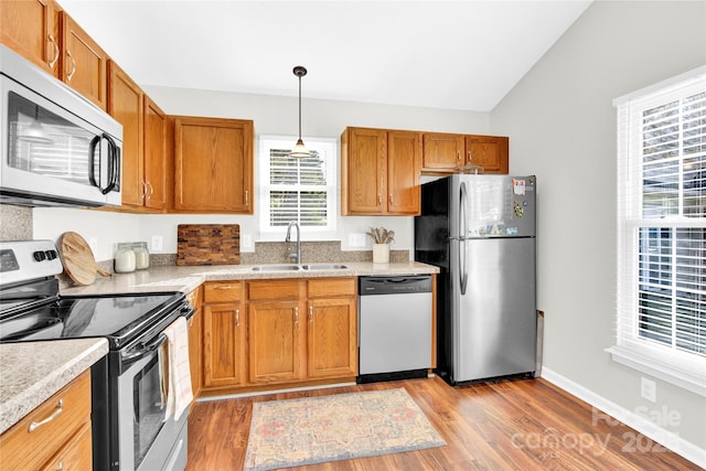 kitchen featuring decorative light fixtures, lofted ceiling, sink, light hardwood / wood-style floors, and stainless steel appliances