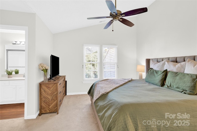 bedroom with vaulted ceiling, connected bathroom, light colored carpet, and ceiling fan