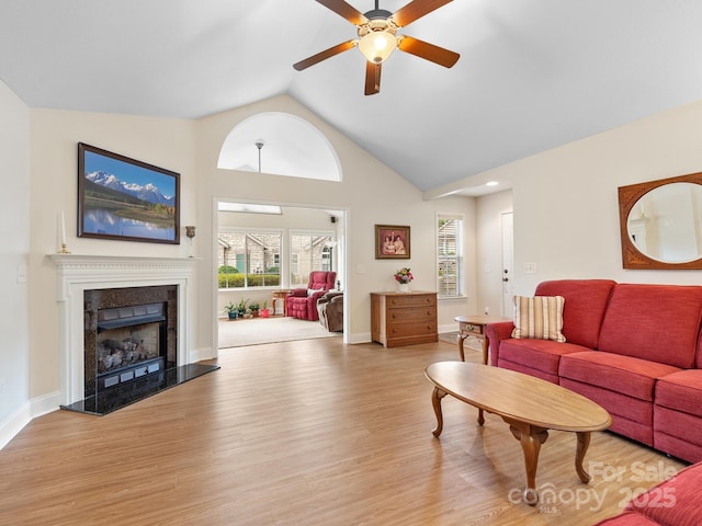 living room featuring a high end fireplace, light hardwood / wood-style flooring, high vaulted ceiling, and ceiling fan