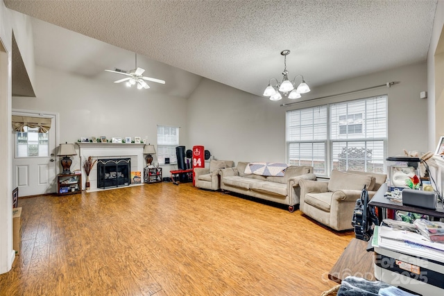 living room featuring lofted ceiling, ceiling fan with notable chandelier, light hardwood / wood-style flooring, and a textured ceiling