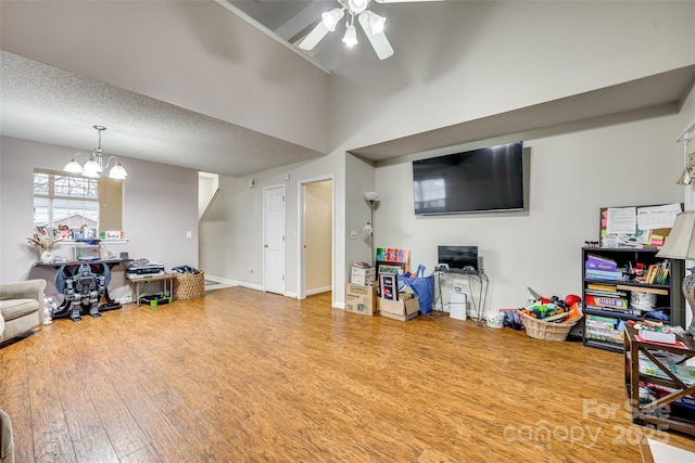 living room featuring hardwood / wood-style flooring, ceiling fan with notable chandelier, a textured ceiling, and a towering ceiling