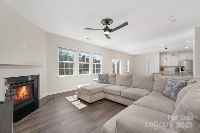 living area with recessed lighting, dark wood-type flooring, a glass covered fireplace, ceiling fan, and baseboards