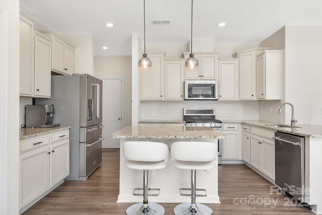 kitchen with pendant lighting, stainless steel appliances, a kitchen island, a sink, and light stone countertops