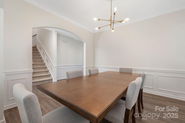 dining area featuring dark wood-type flooring, an inviting chandelier, stairs, crown molding, and a decorative wall