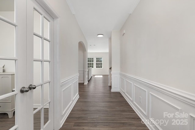 hallway with arched walkways, dark wood-style flooring, and a decorative wall