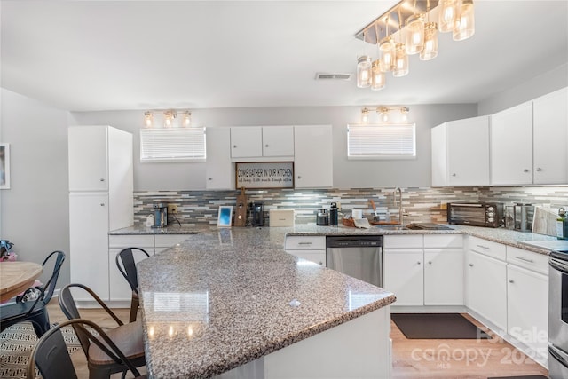 kitchen with appliances with stainless steel finishes, white cabinets, a sink, and decorative light fixtures