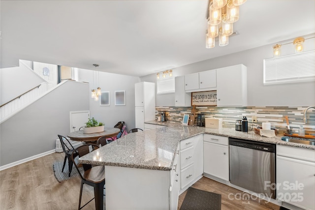 kitchen with a peninsula, a sink, white cabinetry, dishwasher, and decorative light fixtures