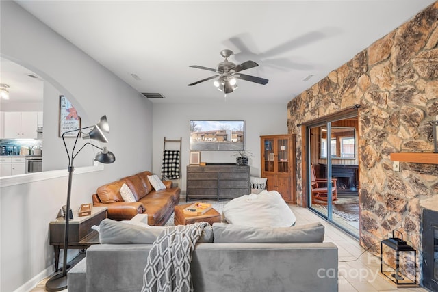 living area with arched walkways, a fireplace, visible vents, and a ceiling fan