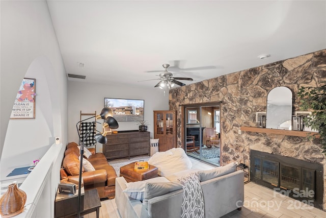 living room with ceiling fan, visible vents, wood finished floors, and a stone fireplace