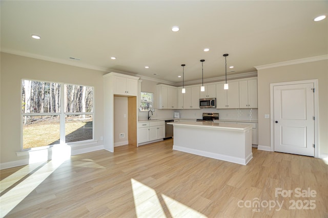 kitchen with stainless steel appliances, white cabinets, light wood-style floors, light countertops, and ornamental molding