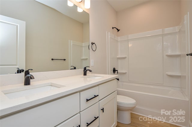 full bathroom with toilet, double vanity, a sink, and wood finished floors