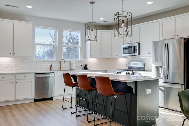 kitchen with a kitchen island, appliances with stainless steel finishes, decorative light fixtures, white cabinetry, and sink