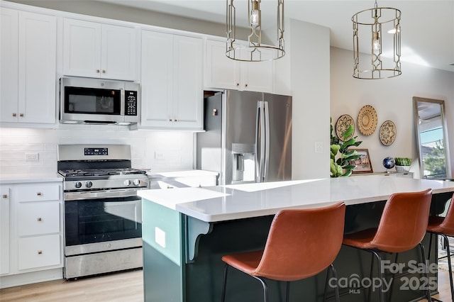 kitchen featuring white cabinetry, appliances with stainless steel finishes, a kitchen island, and hanging light fixtures