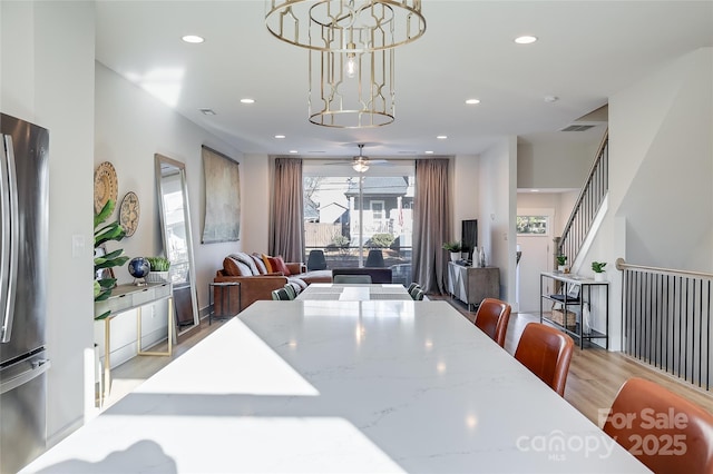 dining space with a wall mounted AC, ceiling fan with notable chandelier, and light wood-type flooring