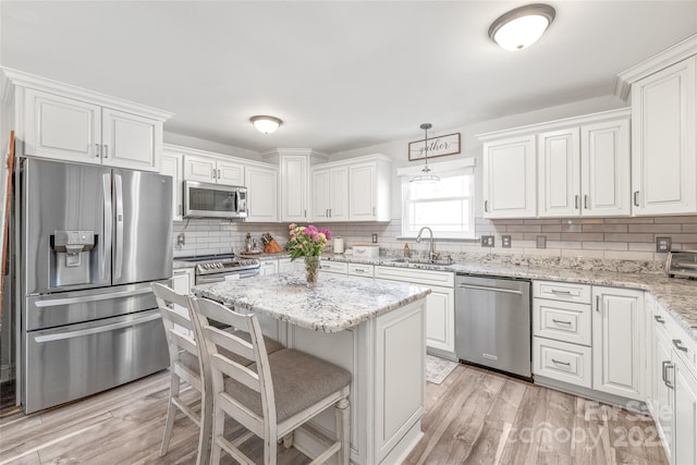 kitchen with pendant lighting, light wood finished floors, appliances with stainless steel finishes, white cabinets, and a sink