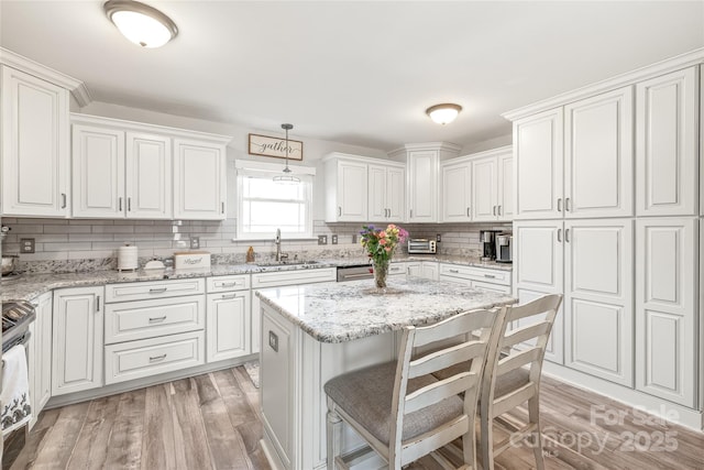 kitchen featuring hanging light fixtures, light wood-style floors, a kitchen island, a sink, and light stone countertops