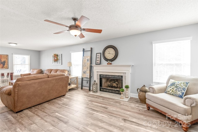 living area featuring light wood-type flooring, a healthy amount of sunlight, ceiling fan, and a premium fireplace