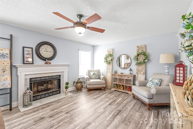 sitting room featuring light wood-style floors, a high end fireplace, ceiling fan, and a textured ceiling