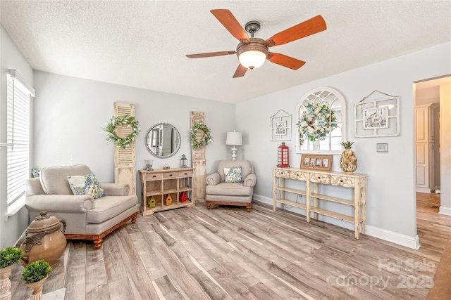 sitting room with a textured ceiling, ceiling fan, baseboards, and light wood-style floors