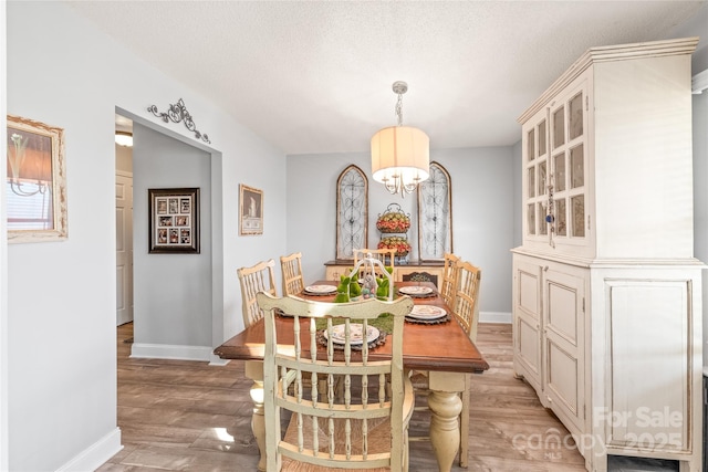 dining space featuring light wood-style floors, a chandelier, a textured ceiling, and baseboards