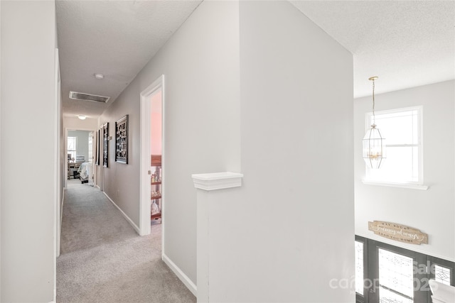 hall with a textured ceiling, light carpet, an upstairs landing, visible vents, and baseboards